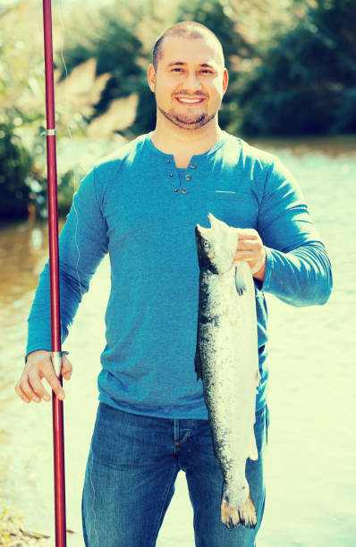 istock fisherman holding fish near wild river 648874168