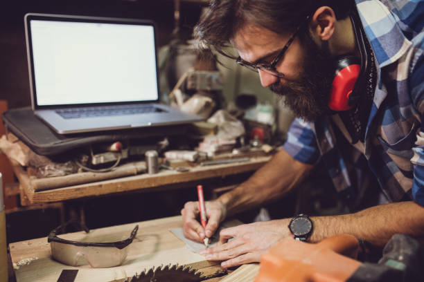 istock Young carpenter writing down measurements in his notebook at workshop 648878786