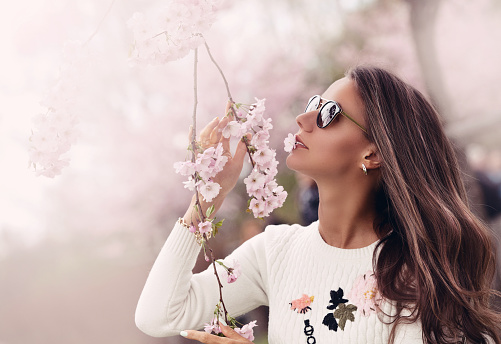 Woman enjoying nature. Girl with sakura tree flowers. Focus on face. Spring concept