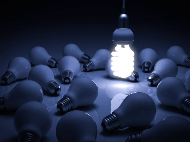 istock Energy saving light bulb , one glowing hanging fluorescent lightbulb standing out from unlit incandescent bulbs on blue background , individuality and different creative idea concepts 648891532