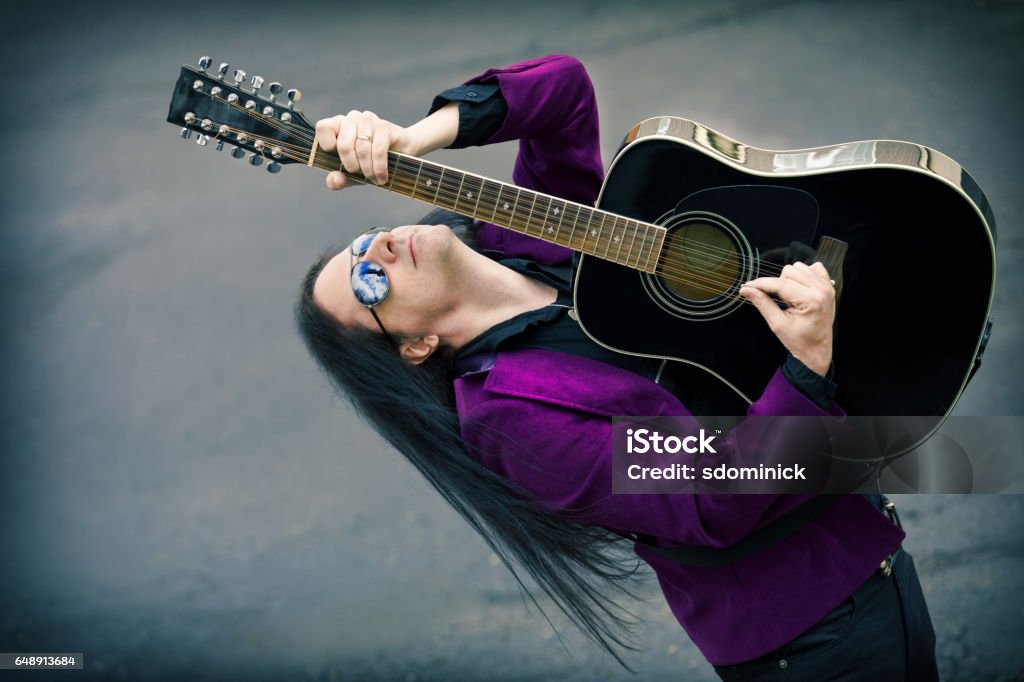 Man Playing 12 String Acoustic Guitar An attractive man with long dark hair playing a 12 string acoustic guitar. Men Stock Photo