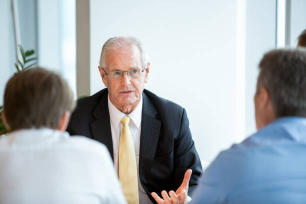 Business Leader Proposing Idea During Negotiations Closeup of senior business man gesturing and talking to two partners who are sitting back to camera old rich white guy stock pictures, royalty-free photos & images