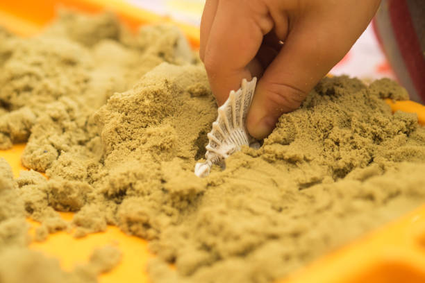 Kid's hand putting dinosaur rubber figure in the sand box stock photo