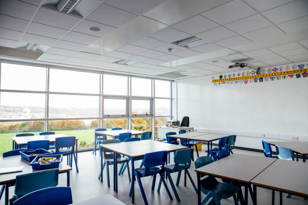 Empty School Classroom Chairs neatly under tables of a school classroom. No People. Large wall of windows empty desk in classroom stock pictures, royalty-free photos & images