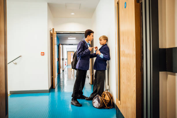 This Student is  a Big Bully Taller boy is pointing his finger at a smaller student while holding onto his top. The smaller boy has his back to the wall and looks worried. They are in a corridor of their school. teasing stock pictures, royalty-free photos & images