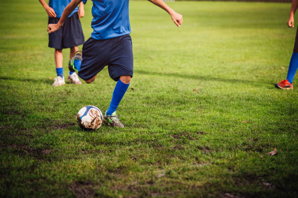 Kicking a Soccer Ball A boy can be seen from the shoulders down kicking a football on a football field. Unrecognisable people sports league stock pictures, royalty-free photos & images
