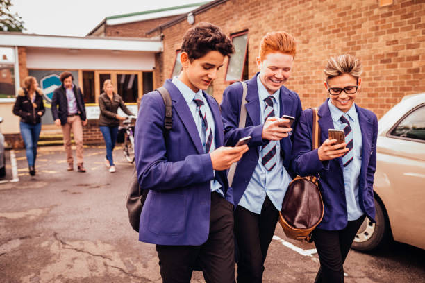 Schoolboys on their Mobile Phones Three schoolboys leaving school with their teachers behind them. They are all on their mobile phones and smiling. secondary school activities stock pictures, royalty-free photos & images