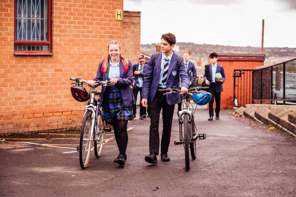 She Cycles to School and Back School children with their bicycles in the school yard. Happy as a girl and boy walk pushing them side by side. bicycle cycling school child stock pictures, royalty-free photos & images