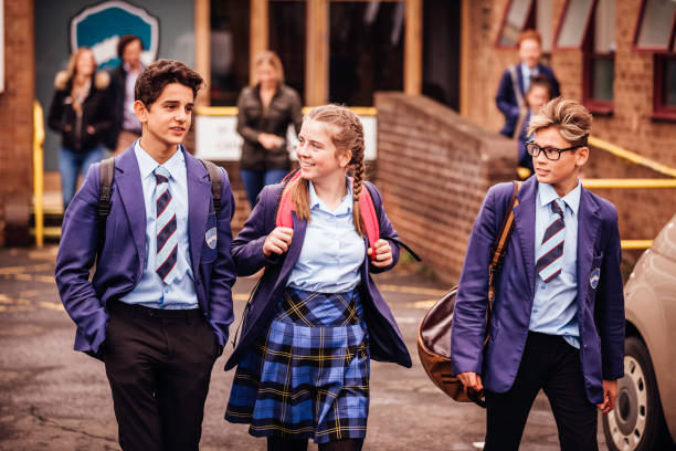 School friends leaving School for the Day Three school friends leaving school with their teachers behind them. They are smiling. school uniform stock pictures, royalty-free photos & images