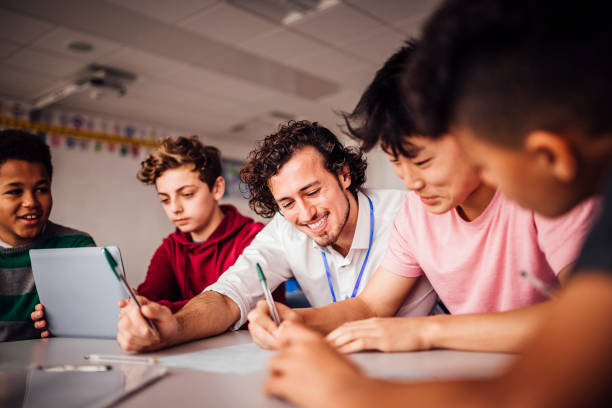 Enjoying School Work Together Teacher helping students with their schoolwork. The student looks happy as they sit side by side at a table. Another student looks at a digital tablet. male chinese student stock pictures, royalty-free photos & images