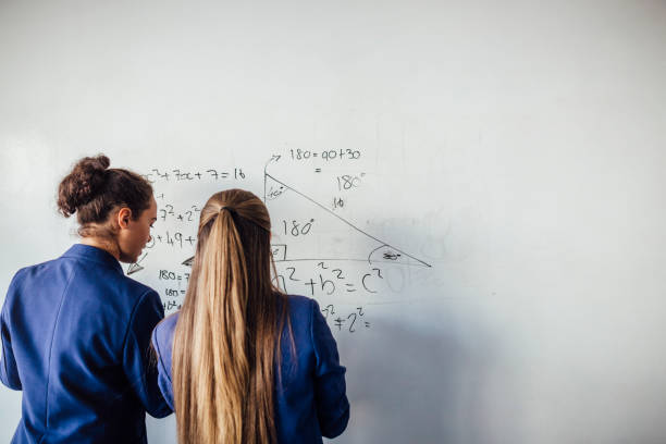 She loves Mathematics Two teenage school girls standing in front of  a large whiteboard side by side solving a mathematics equation on the board. Back view mathematical symbol stock pictures, royalty-free photos & images