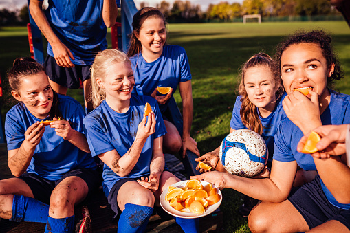 Young teenage girls sitting down to eat some fresh sliced oranges. Dirty sitting with a soccer ball and all smiling