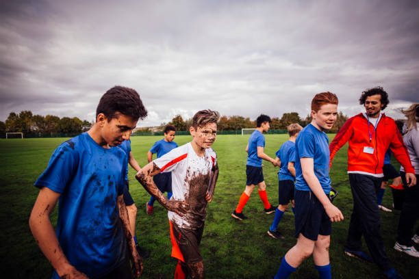 Another Successful Game Teenage boys walk off a sports field looking happy and dirty. Their coach is smiling. rugby team stock pictures, royalty-free photos & images