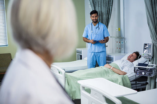 Doctor and surgeon interacting in ward while consulting patient