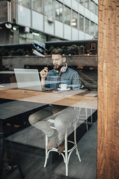 istock Hipster man in cafe working on laptop by window 648950486