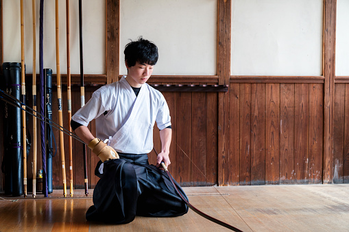 Young adult male pauses to show his respect before starting his practice of the traditional Japanese sport of Kyudo, archery. Okayama, Japan. March 2017