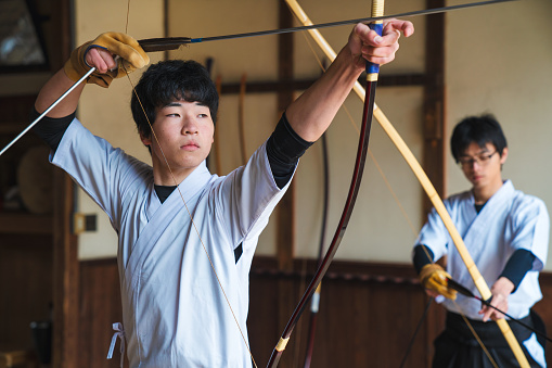 Traditional Japanese archery follows a set pattern with the archer pausing with the arrow above their eye line as they prepare for the shot. Once they are mentally prepared the arrow is lowered to the eye level of the archer as he takes aim. Okayama, Japan. March 2017