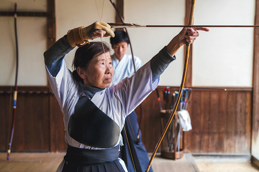 Traditional Japanese archery follows a set pattern with the archer pausing with the arrow above their eye line as they prepare for the shot. Once they are mentally prepared the arrow is lowered to the eye level of the archer as she takes aim. Okayama, Japan. March 2017