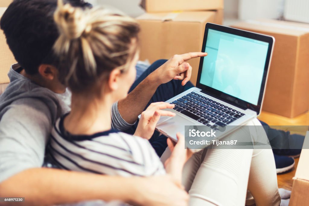 Jovem casal sentado entre caixas e usando um laptop - Foto de stock de Casal royalty-free