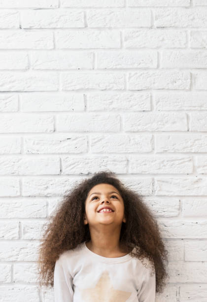 Cute girl over a white brick wall looking up