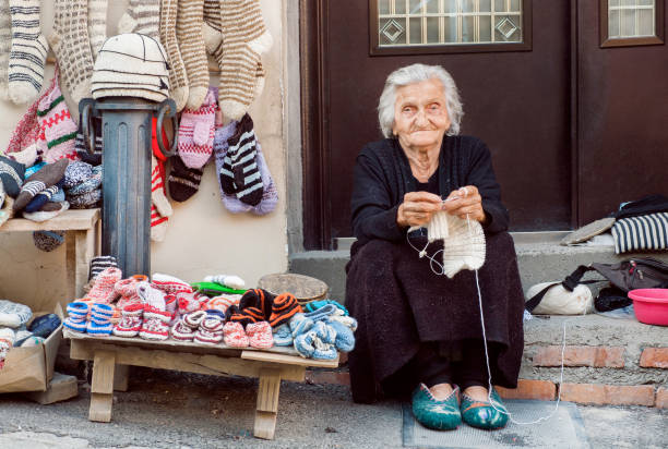 mujer senior con sentado en la puerta de casa y agujas de tejer calcetines de lana para la familia - women poverty senior adult mature adult fotografías e imágenes de stock