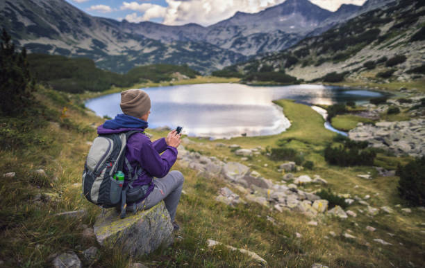 istock Traveler using a smart phone in mountains sitting near lake 648984050