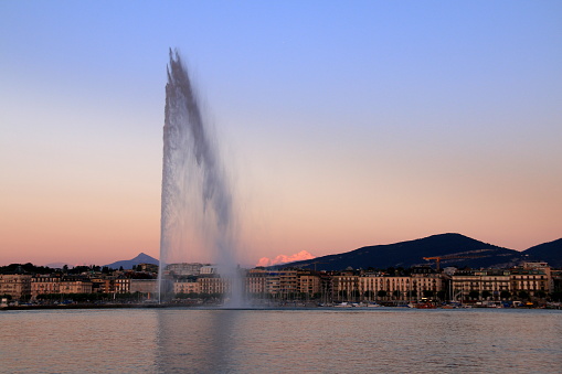 Silhouette of the wind blown jet d'eau and red color of the snow in the Alps after sunset in Geneva in Switzerland.