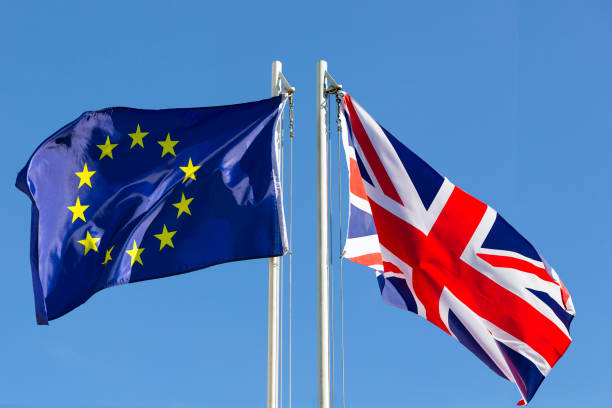 European Union and United Kingdom flags waving on flagpoles against a clear blue sky.
