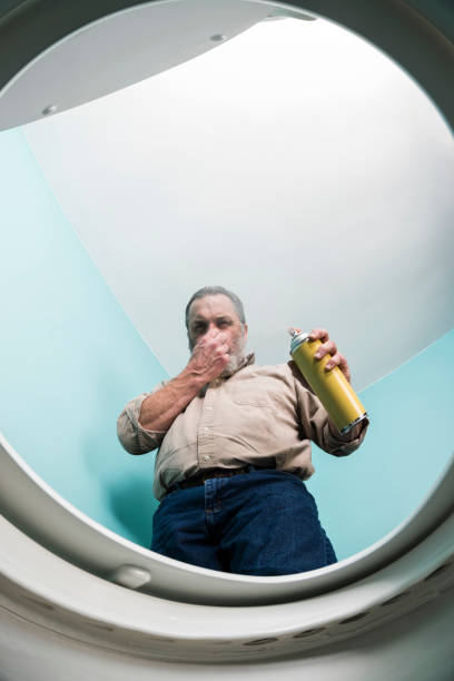Looking up at man spraying air freshener into smelly toilet Looking up from inside the toilet bowl as adult male is spraying a yellow aerosol can of air freshener in to a toilet. He is holding his nose to protect himself from the foul smell coming from the toilet. He is wearing casual clothes, that include a tan button down shirt and blue jeans. holding nose stock pictures, royalty-free photos & images