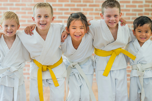 A group of elementary age children are taking a martial arts class. They are standing together in a row and are smiling while looking at the camera.