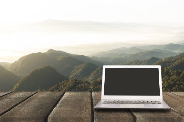 istock Laptop with blank screen on wooden table with forest in mountain and pine trees background, can used for display or montage your products 649070488