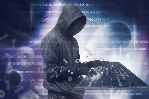 Hooded hacker man with anonymous mask typing on virtual keyboard over binary code background