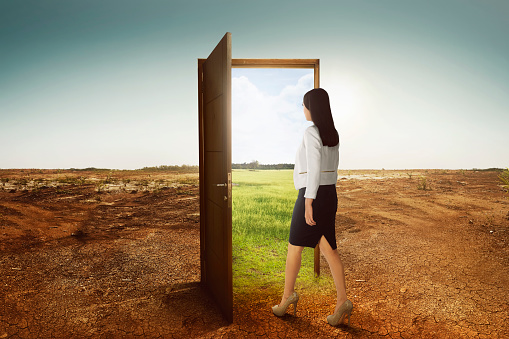 Young asian business woman walking to the open door going to green environment on cracked land background