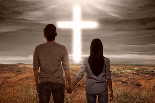 Asian couple holding hand each other looking bright cross shape on the sky
