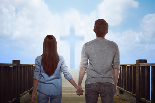 Asian couple looking at bright cross sign on the daylight