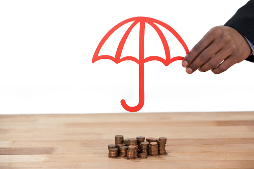 Hand protecting stack of coins with umbrella at desk