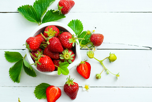 fresh ripe and under ripe strawberry fruits, flowers, leaves on white wood table background
