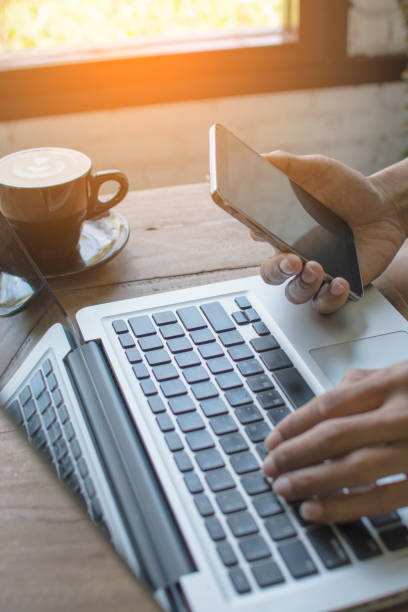 istock Hands holding mobile phone and working on computer typing laptop keyboard using wifi cyber internet online for business communication 649160140