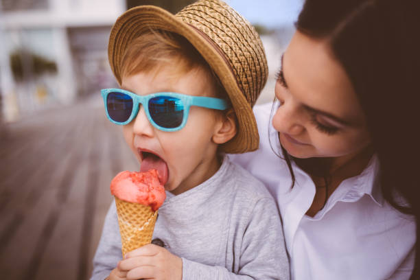 chico joven lindo comer helado en brazos de su madre - ice cream licking little boys ice cream cone fotografías e imágenes de stock