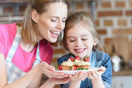 portrait of smiling mother and daughter holding homemade cupcakes with strawberries