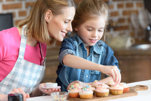 istock side view of daughter and mother decorating cupcakes with confetti 649191128