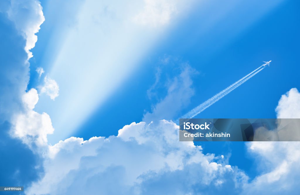 Avión que volaba en el cielo azul entre las nubes y la luz del sol - Foto de stock de Avión libre de derechos