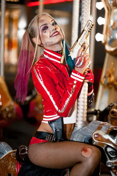 Portrait of smiling cosplayer girl in costume Harley Quinn on background lights of carousel ride. Close-up. Cosplay