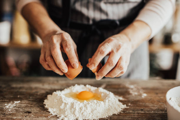 mujer añade un huevo a la harina - making fotografías e imágenes de stock