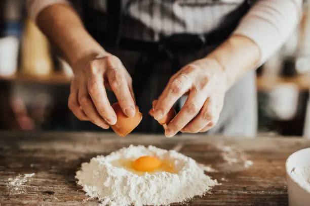 Photo of Woman adds an egg to the flour