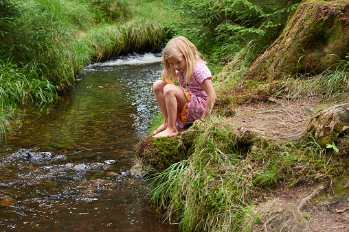 Child cute blond girl playing in the creek. Summer children fun.