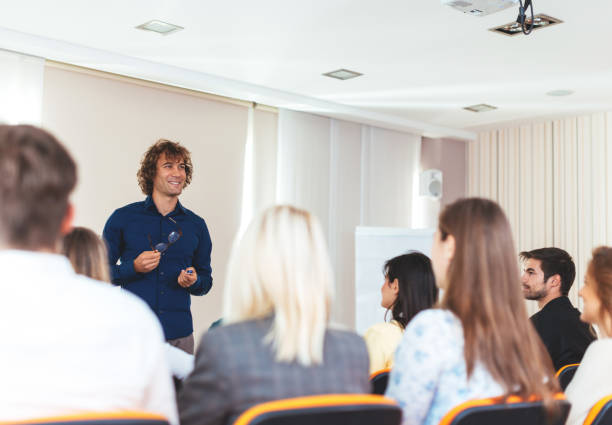 istock Young coach holding speech on conference with many young participants 649205504