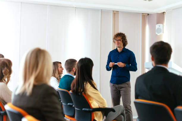 istock Young coach holding speech on conference with many young participants 649206952
