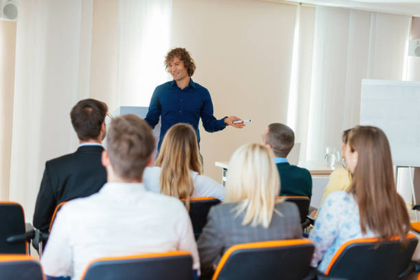 istock Young coach holding speech on conference with many young participants 649214252