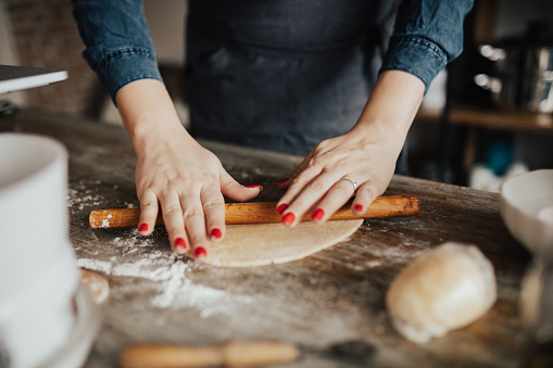 Close-up of young woman kneading dough with rolling pin